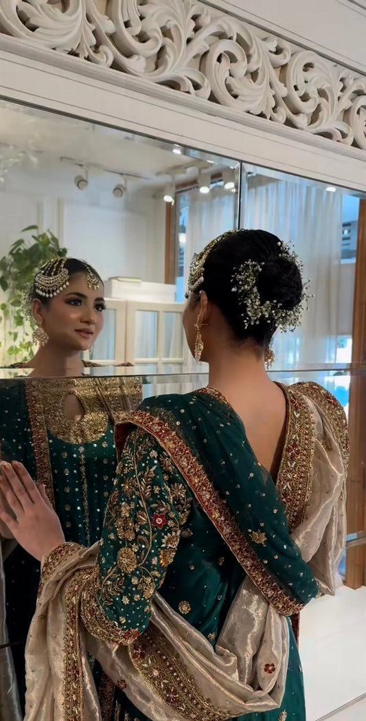  Mehru deep emerald ensemble featuring antique gold and subtle maroon accents with a matching green dupatta edged in ornate red and maroon borders, creating a regal look steeped in timeless tradition and quiet grandeur.