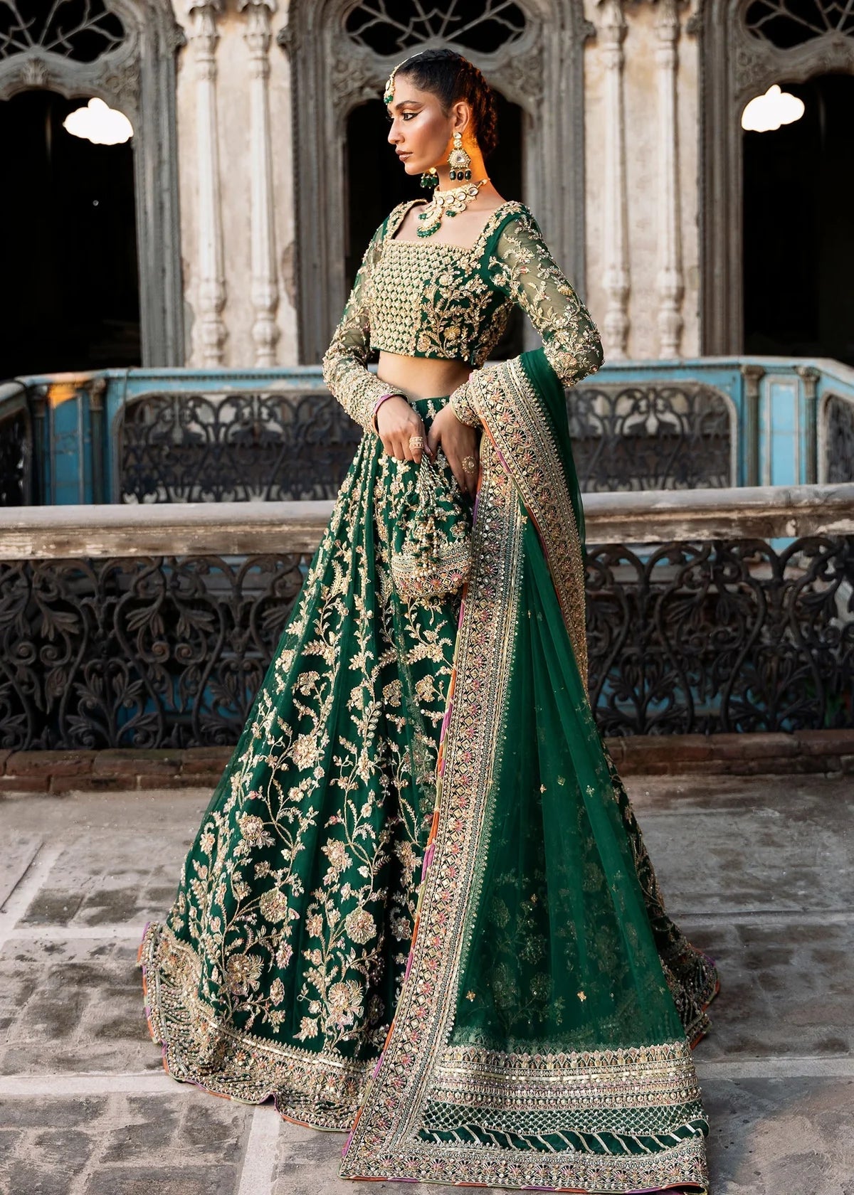  Kanwal Malik Sukhan bottle green net lehenga choli featuring an intricately embellished choli and flowing lehenga with a floral jaal design in vibrant orange and pink accents, enhanced with gold, gotta, and silver embellishments, complete with a matching net dupatta with an embellished border, perfect for weddings and festive occasions.