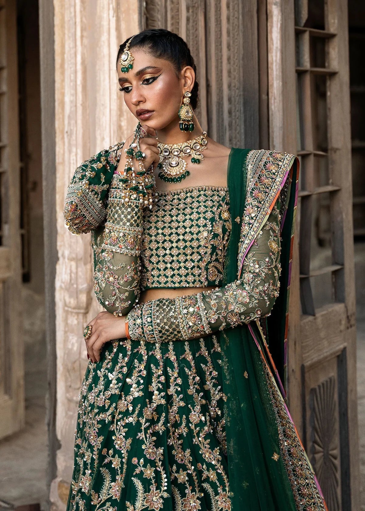  Kanwal Malik Sukhan bottle green net lehenga choli featuring an intricately embellished choli and flowing lehenga with a floral jaal design in vibrant orange and pink accents, enhanced with gold, gotta, and silver embellishments, complete with a matching net dupatta with an embellished border, perfect for weddings and festive occasions.