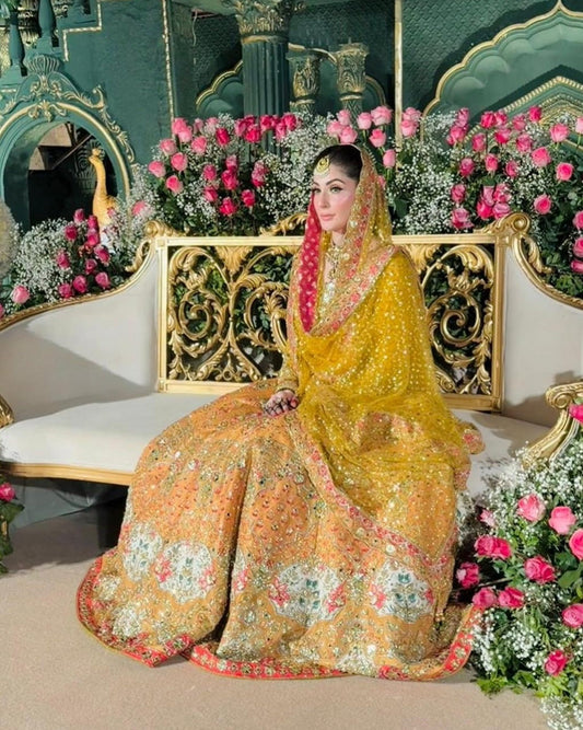Luxury mustard yellow bridal lehenga choli featuring intricate hand embellishments with detailed floral embroidery in soft pastel hues along the lehenga border, paired with a heavily adorned net dupatta with contrasting pink and gold border and a finely embellished choli, perfect for mehndi, mayun, dholki, and wedding festivities.