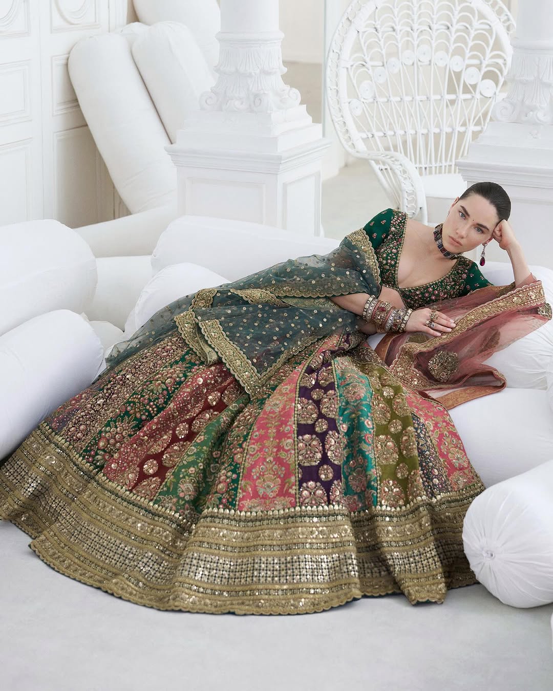 Sabya Sachi Mukherjee multi-color bridal lehenga choli featuring a deep emerald green embellished choli paired with a richly crafted lehenga showcasing intricate gold embroidery and panelled patterns in maroon, purple, pink, and green hues, with a heavily adorned lehenga border detailed in fine zari, sequins, and handcrafted embellishments, completed with a sheer embellished dupatta with gold detailing, perfect for barat, reception, walima, and grand festive occasions.